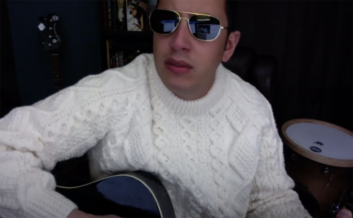 a man wearing sunglasses and a white sweater is playing a guitar