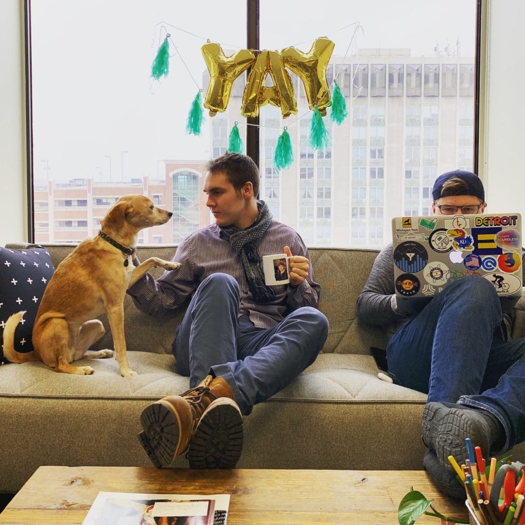 two men sit on a sofa next to a brown dog in the Nutshell office