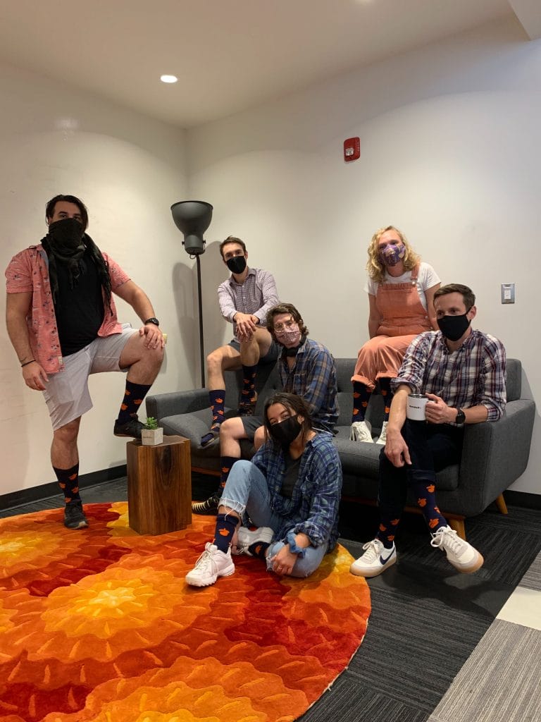 Nutshellers wearing face masks and colorful socks pose for a picture on a sofa