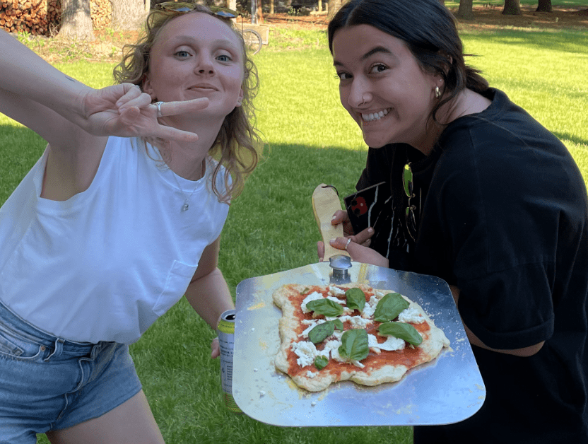 Nutshellers Madi and Hana standing next to each other holding a pizza